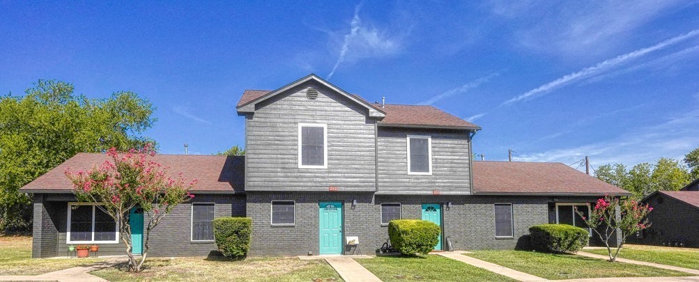 a gray house with blue doors and a blue sky