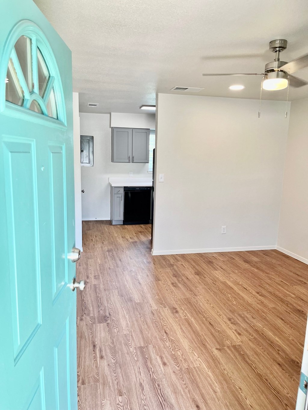 an empty living room and kitchen with wood flooring and a blue door