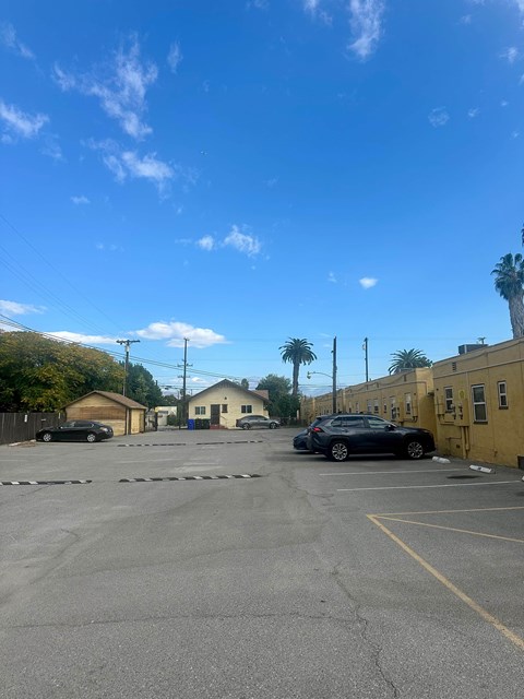 A parking lot with a car parked in the foreground and a yellow building to the right.