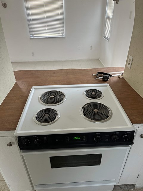 A white stove top oven with four burners and a black control panel is in a kitchen with a wooden counter top.