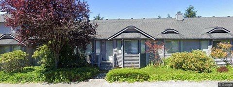 A house with a grey roof and a tree with red leaves in front.
