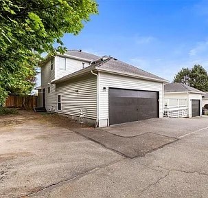 A two-story house with a garage door is surrounded by a driveway and trees.