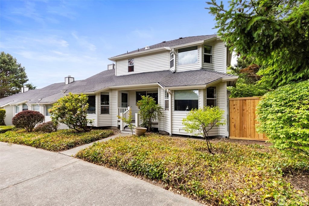 A house with a grey roof and white walls with a brown fence and bushes in front.