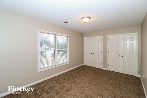 a bedroom with carpet and two closets and a window