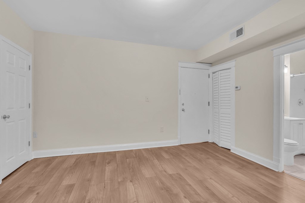 a bedroom with white walls and wood flooring and a door to a bathroom