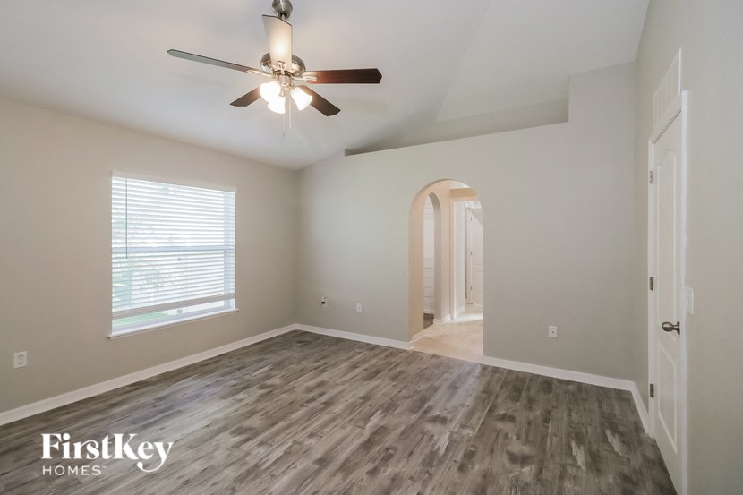 an empty living room with a ceiling fan and a door to a hallway