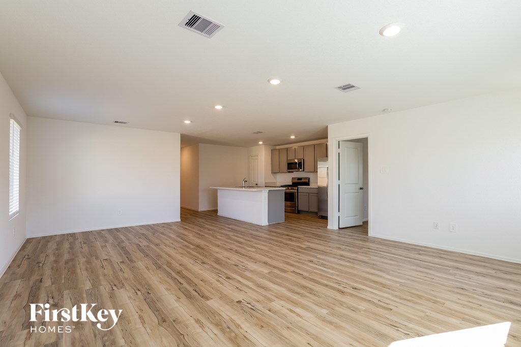 A spacious room with wooden flooring and a kitchen area in the background.