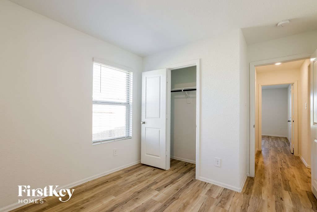 A room with wooden floors and white walls, with a window on the left and a door on the right.