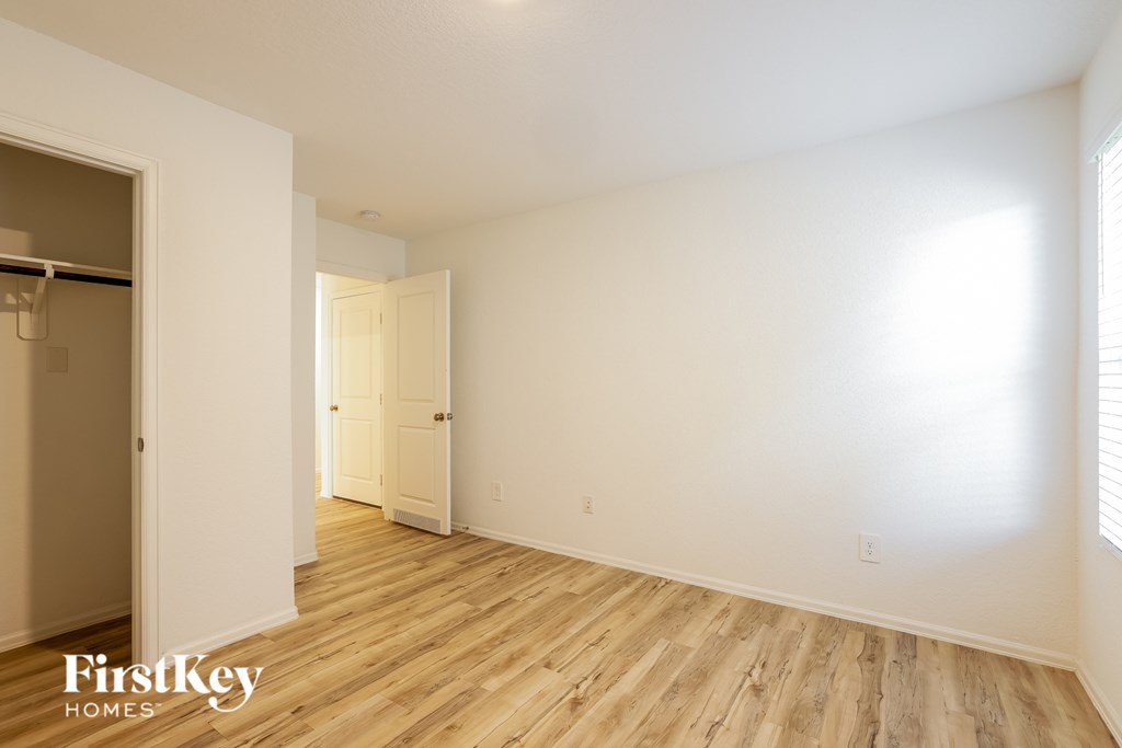 A room with wooden floors and white walls, with a door on the left and a window on the right.