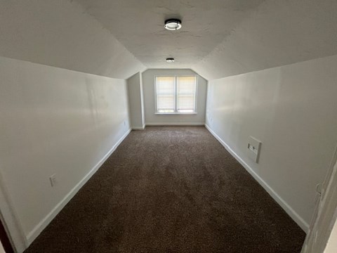 A long, empty hallway with a carpeted floor and a window at the end.