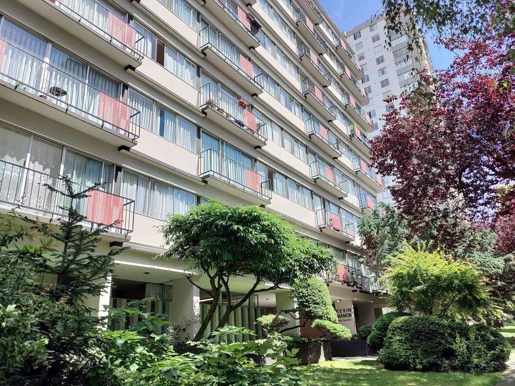 A tall building with balconies and trees in front.