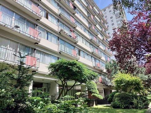 A tall building with balconies and trees in front.