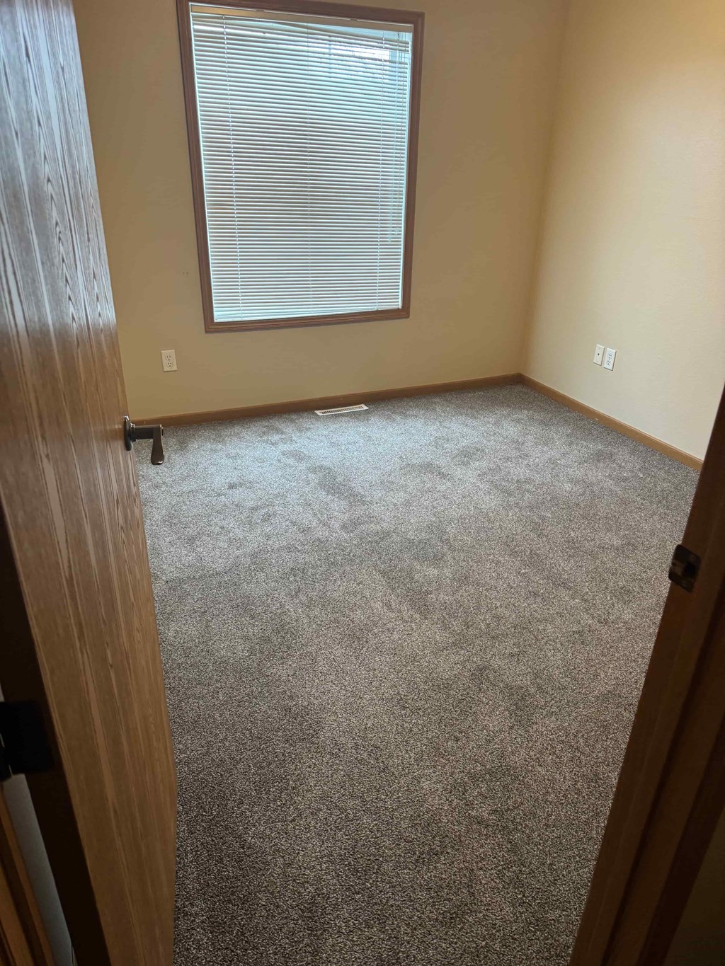 A room with a carpeted floor and a window with blinds.