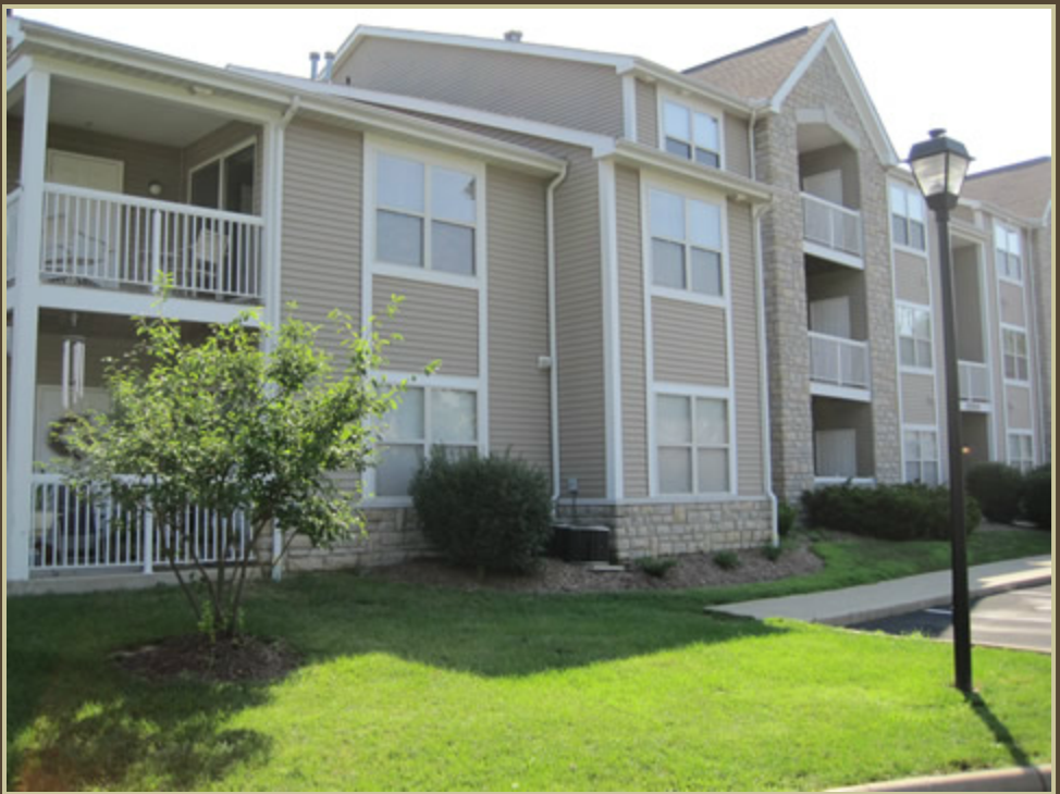 the exterior of an apartment building with green grass and a sidewalk