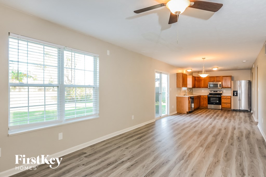 an empty living room and kitchen with wood flooring and a ceiling fan