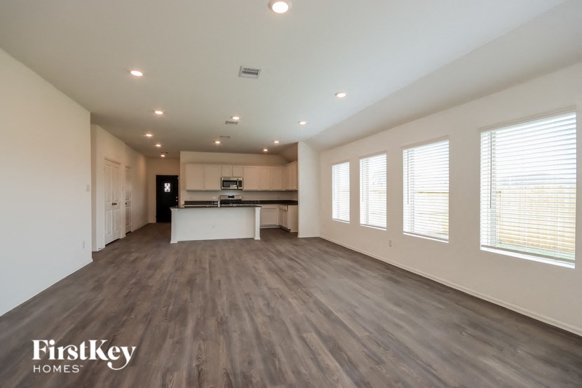 an empty living room with a kitchen and a large window