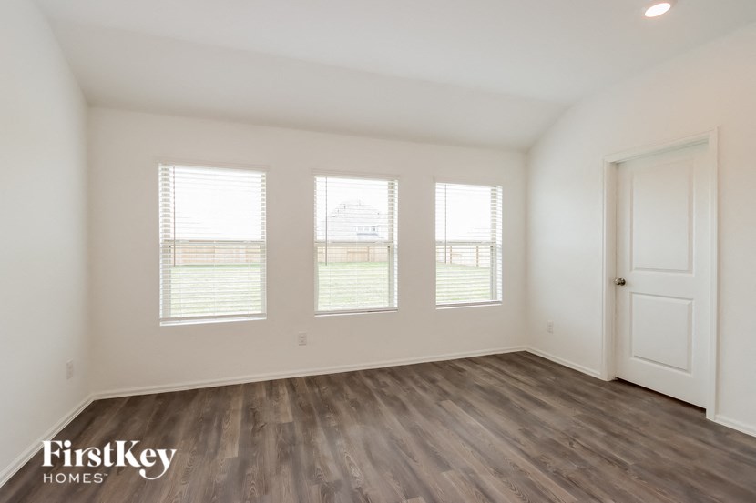 the living room of an apartment with wood flooring and three windows