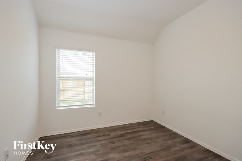 a bedroom with white walls and wood flooring and a window