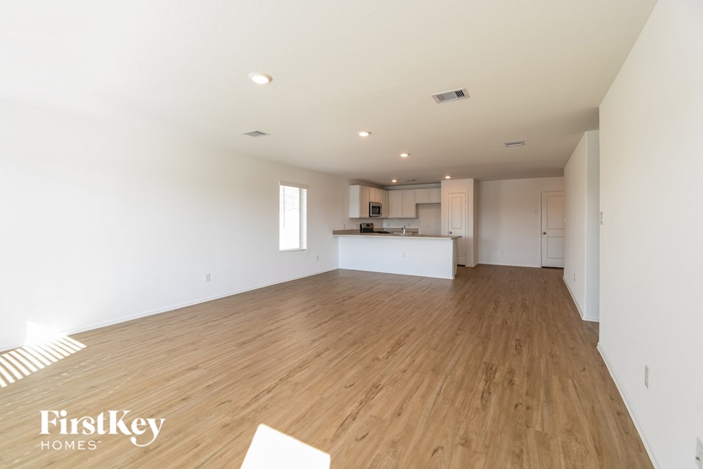 A spacious room with wooden flooring and a kitchen area in the background.