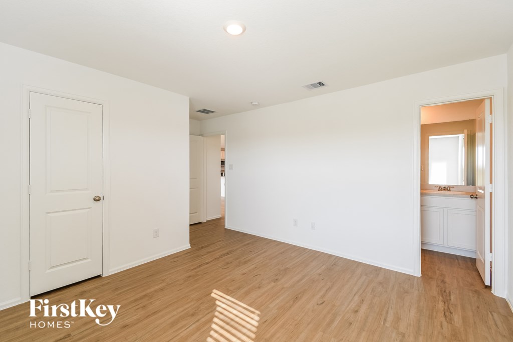 A room with wooden floors and white walls, with a door on the left and a window on the right.