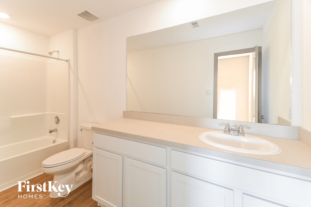 A white bathroom with a toilet, sink and mirror.