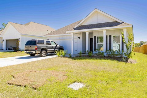 A white house with a grey car parked in front.