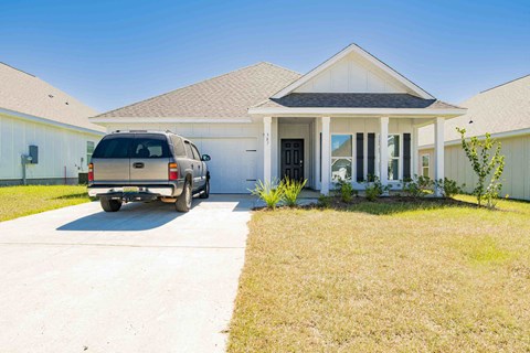 A tan station wagon is parked in front of a white house.