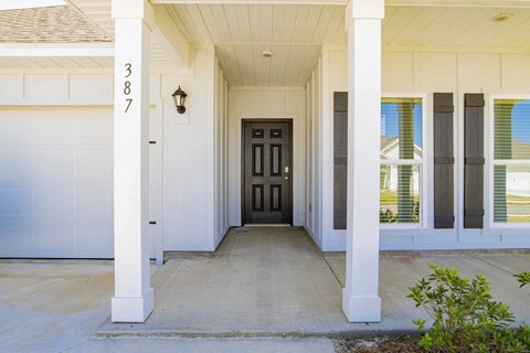 A white house with a black door and a lamp on the wall.
