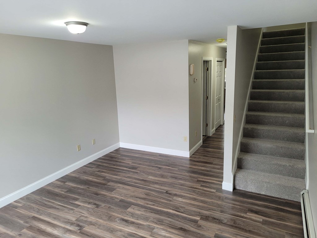a living room with a staircase and a white wall and wood floors