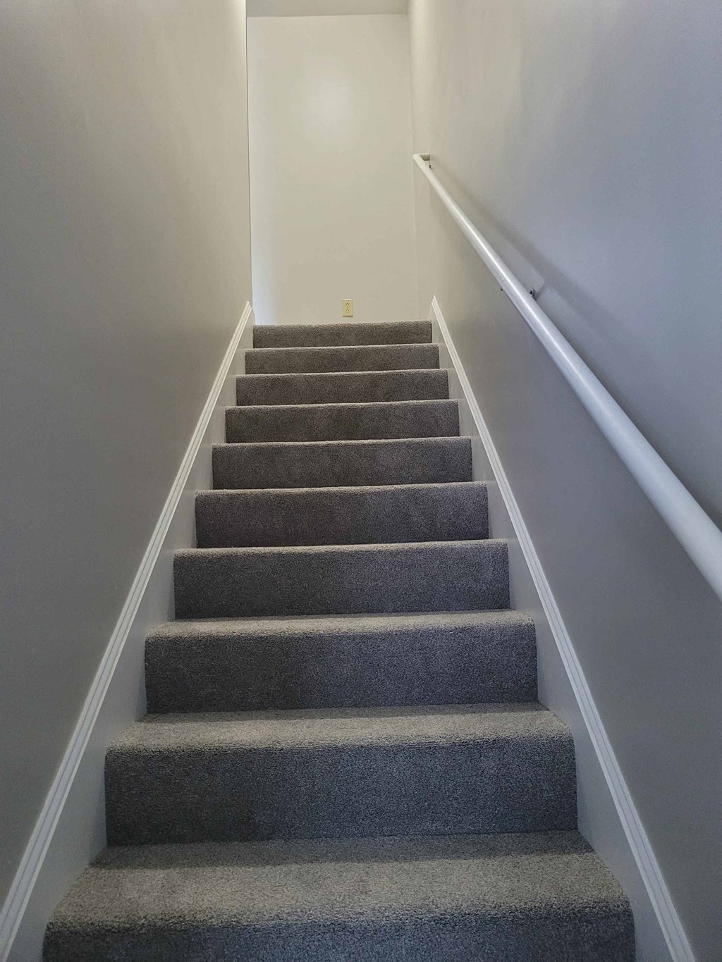 a set of stairs leading up to a white wall and gray carpeted stairs