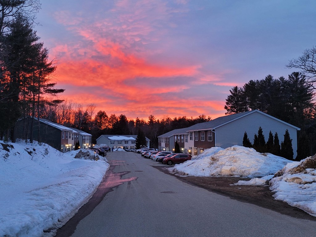 a street at sunset in a snow covered neighbourhood with cars parked