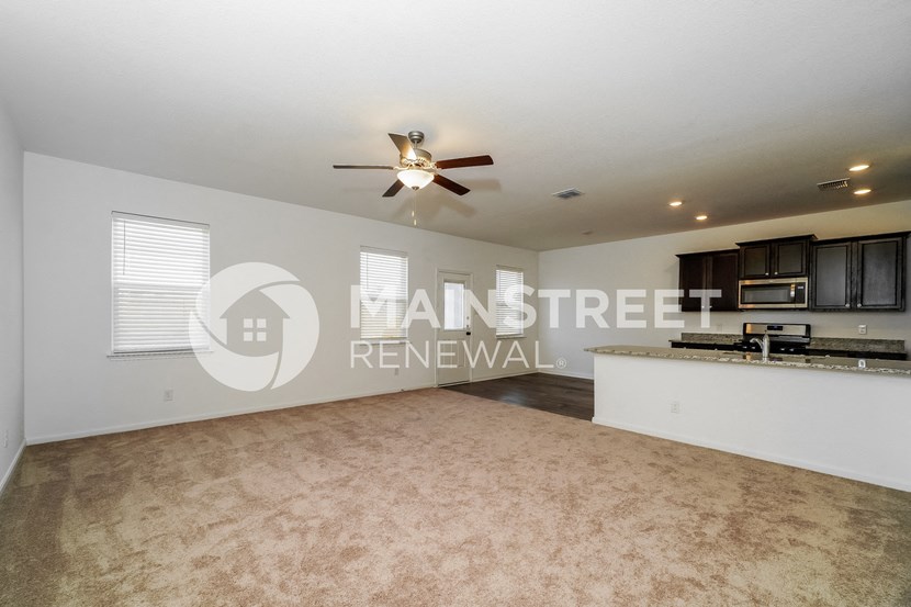 a living room with a kitchen and a ceiling fan