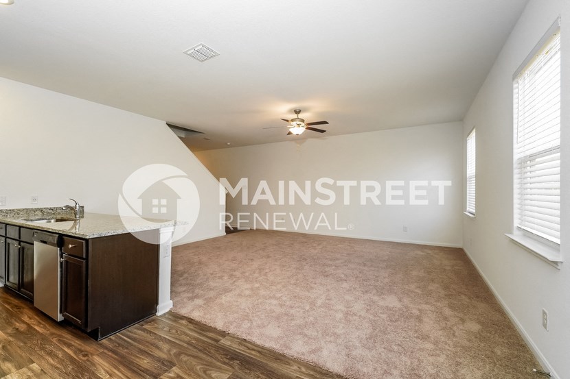 a living room with a kitchen and a ceiling fan