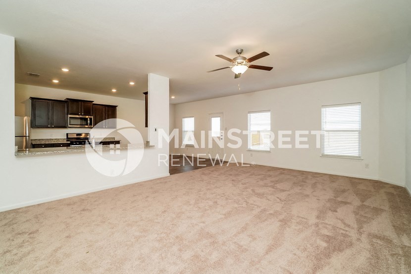 a large living room with a ceiling fan and a kitchen
