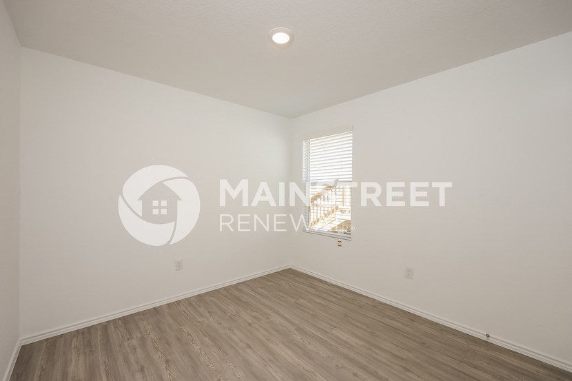 a bedroom with white walls and wood flooring and a window
