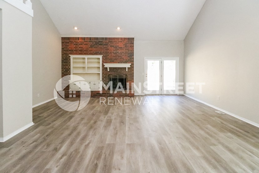 a renovated living room with wooden floors and a brick fireplace