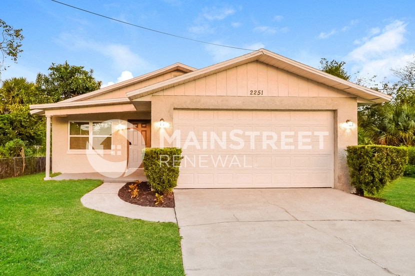 a small tan house with a driveway and grass
