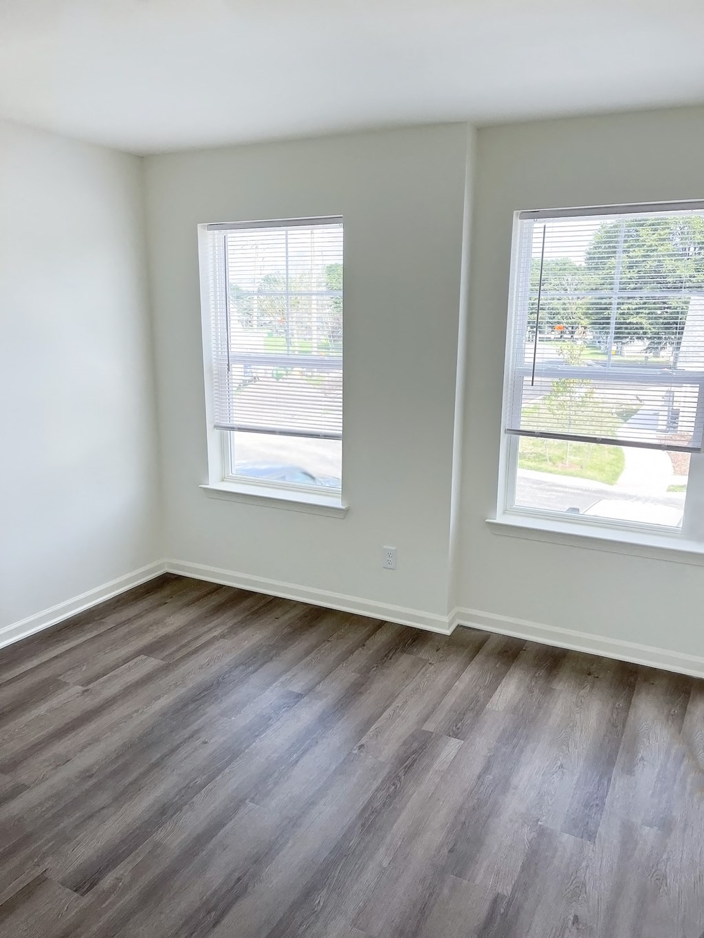 an empty room with wooden floors and two windows