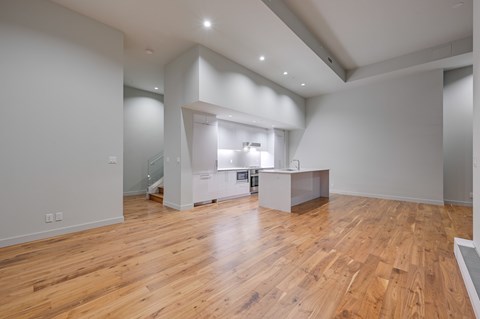 A spacious room with wooden floors and a kitchen area in the background.