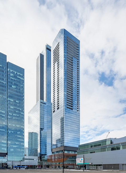 A tall glass skyscraper stands in front of other buildings.