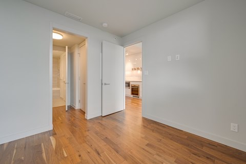 A room with white walls and wooden floors with a doorway leading to another room.