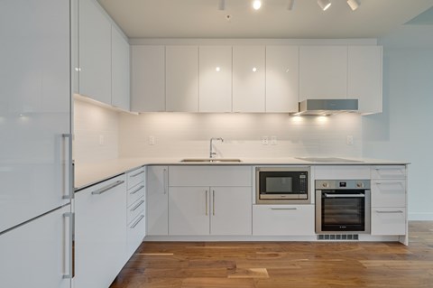 A modern kitchen with white cabinets and a wooden floor.