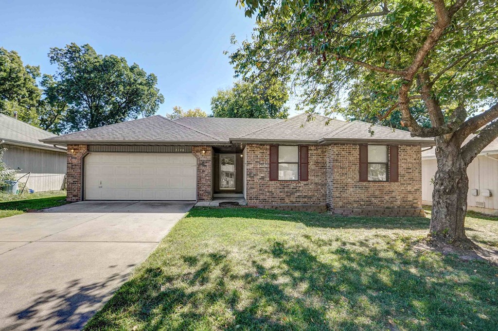 the front of a brick house with a garage and a tree