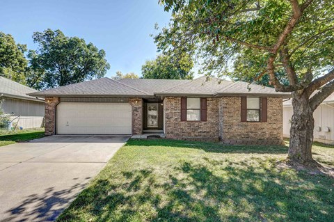 the front of a brick house with a garage and a tree