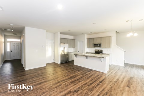 A spacious, well-lit kitchen and living room with wooden floors and white walls.