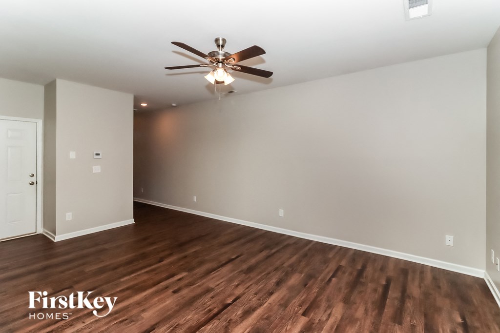 the spacious living room with hardwood flooring and a ceiling fan