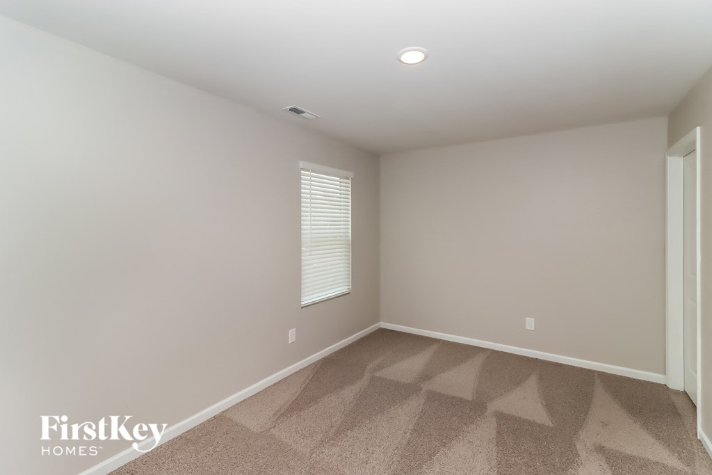the second bedroom has a large window and beige walls and carpet