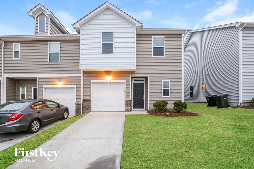 A grey car is parked in front of a two-story house with a garage.