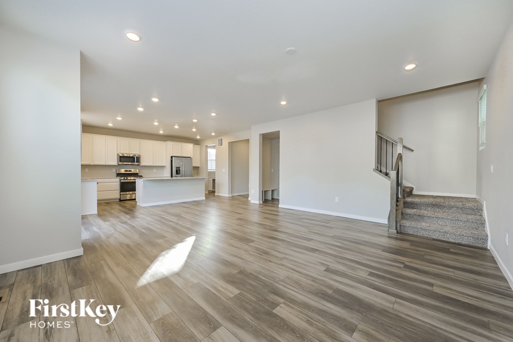 A spacious living room with wooden flooring and a staircase leading to the upper level.