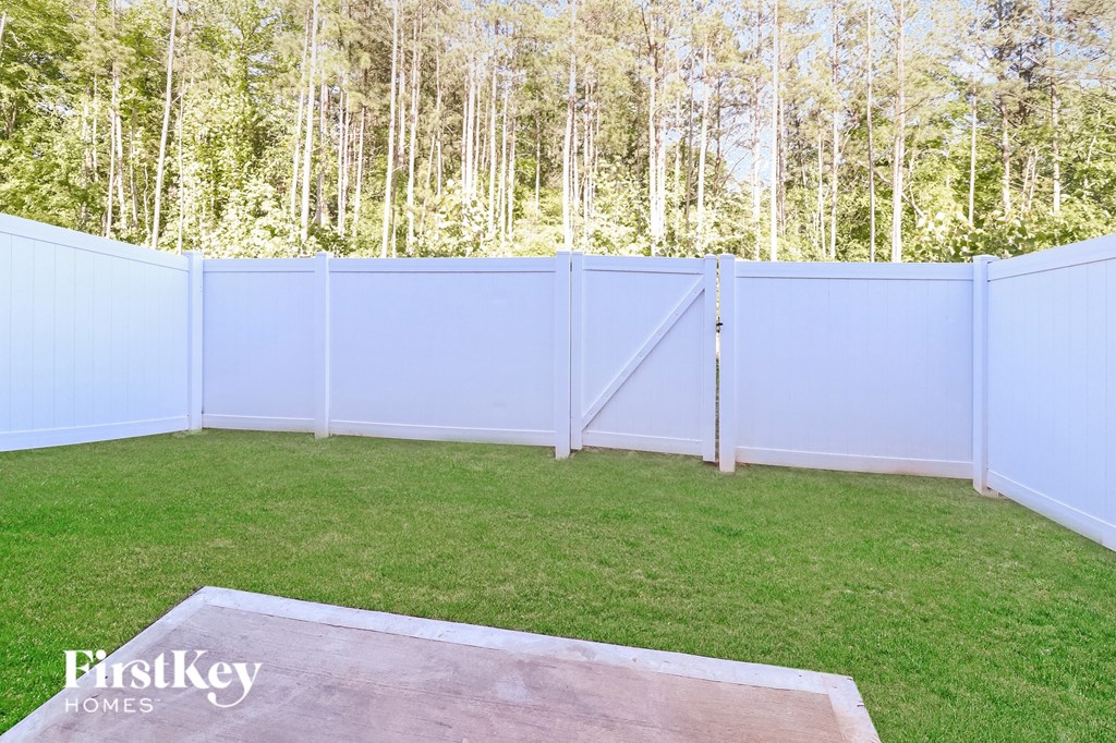 A backyard with a white fence and a wooden deck.